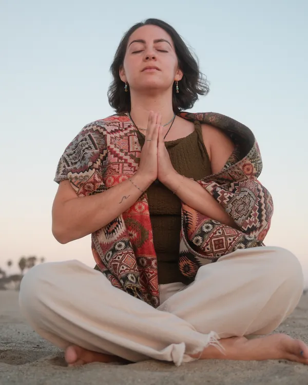 Nicole Sanchez meditating cross-legged on the sand at dusk, hands in prayer, eyes closed