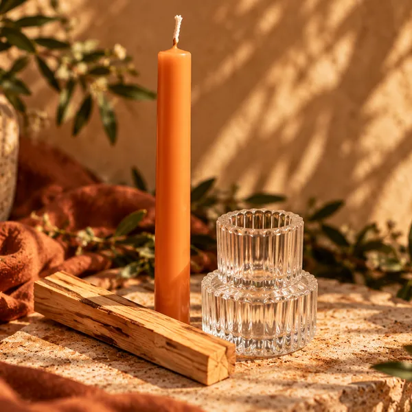 Release & Renew Ritual Kit: an orange taper candle, a ribbed glass candle holder and a palo santo stick in warm sunlight